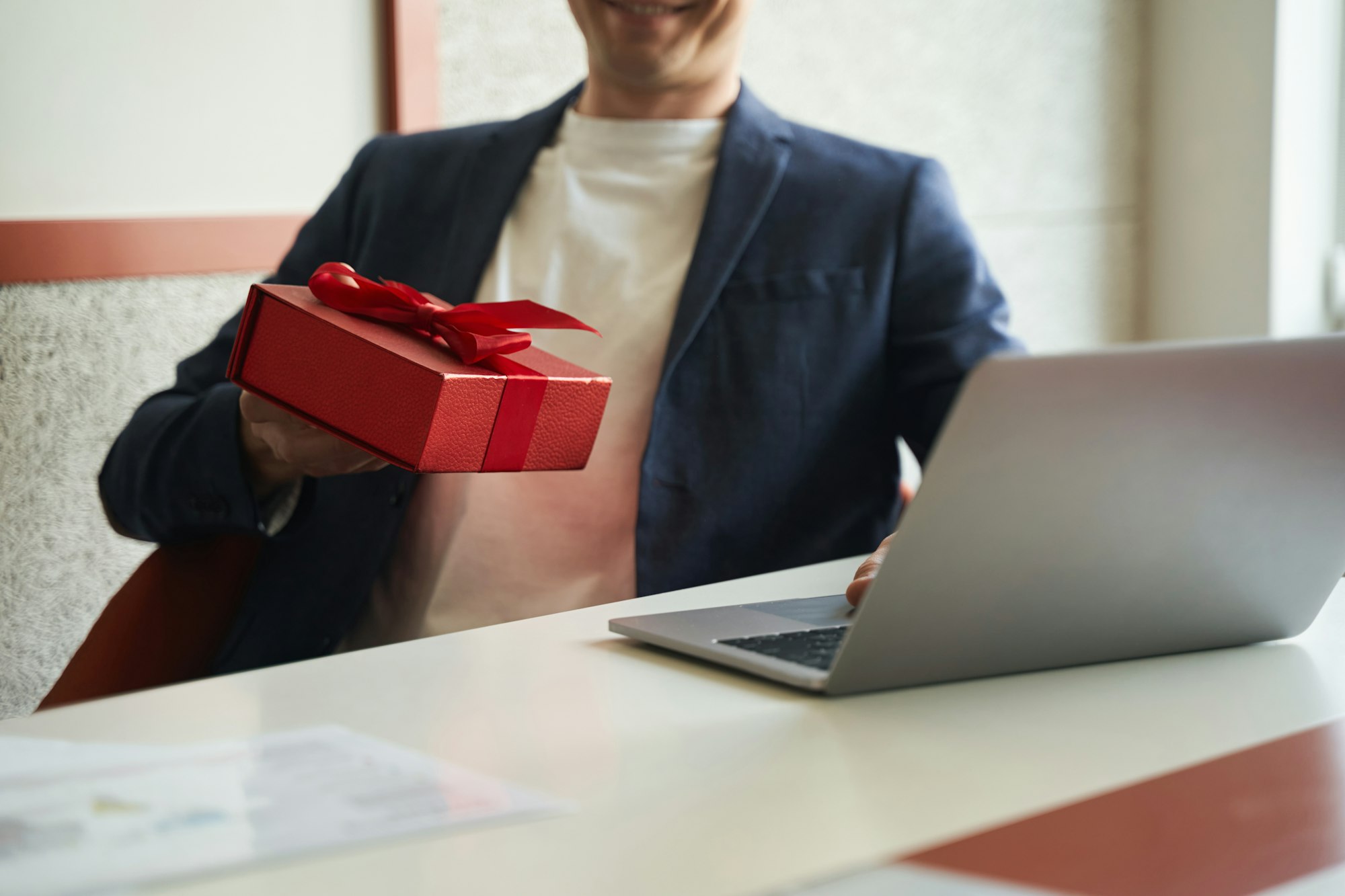 Red giftbox in hand of businessman before laptop