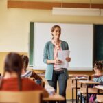 Happy elementary school teacher giving lecture to her students in the classroom.