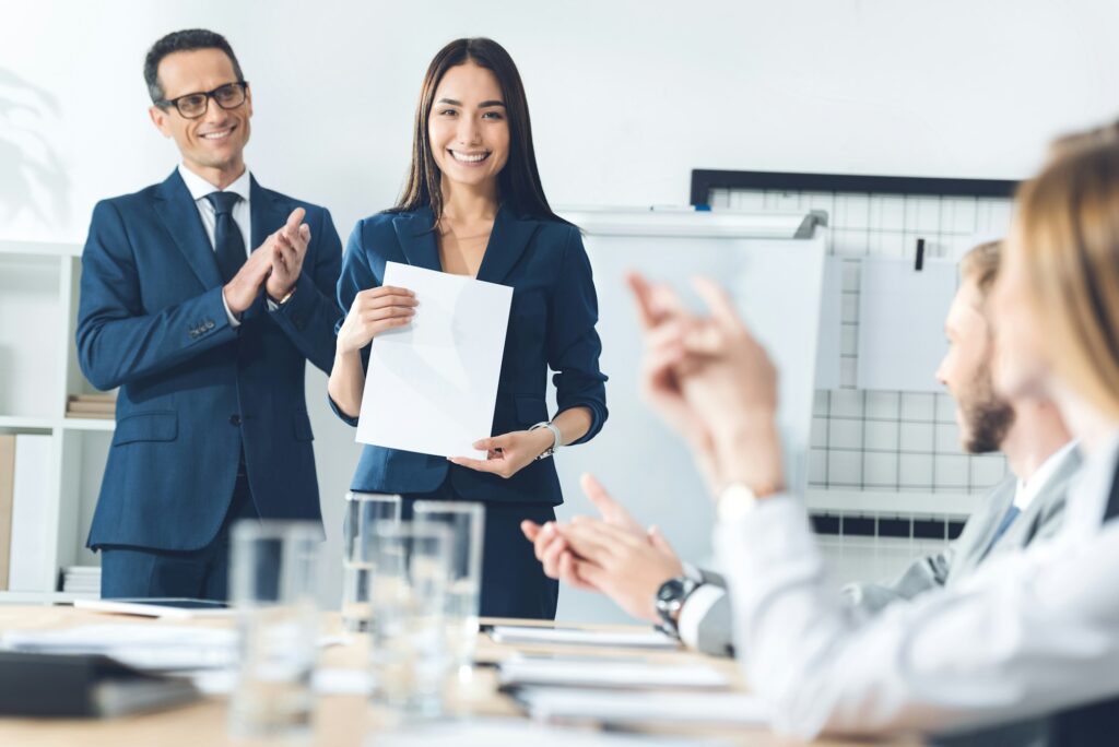 rewarded happy manageress holding blank paper while colleagues clapping to her